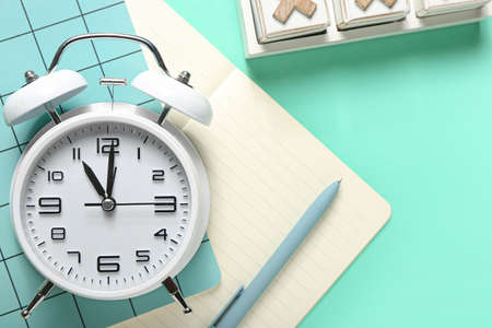 Alarm clock, notebooks and pen on color background, closeup