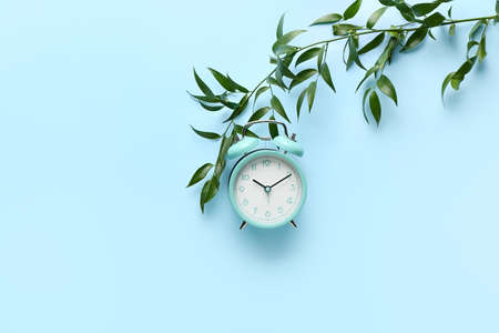 Alarm clock and green branch on color backgroundの写真素材