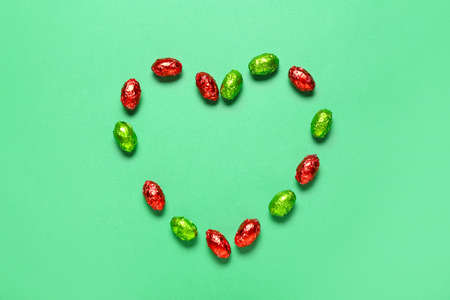 Heart made of sweet chocolate eggs on color backgroundの写真素材