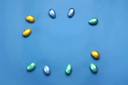 Frame made of sweet chocolate eggs on color background