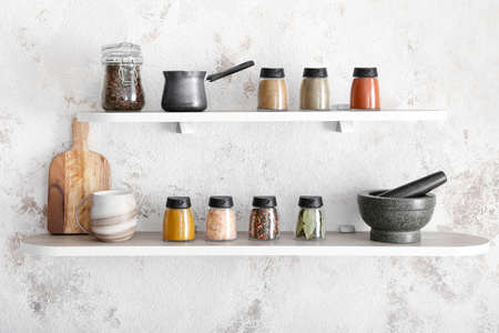 Jars with different spices, coffee beans and kitchen utensils on shelvesの写真素材