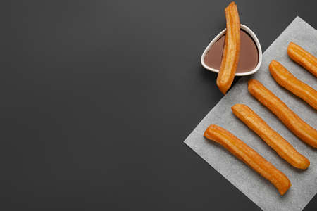 Parchment with tasty churros and melted chocolate sauce on dark backgroundの写真素材