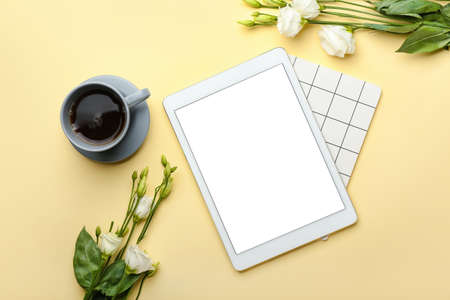 Cup of coffee, tablet computer, notebook and flowers on color background