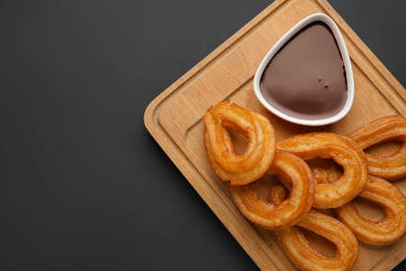 Board with tasty churros and melted chocolate sauce on dark backgroundの写真素材
