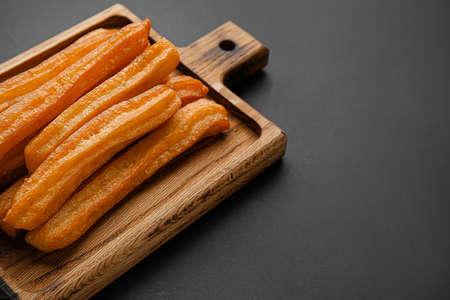 Board with tasty churros on dark background, closeupの写真素材