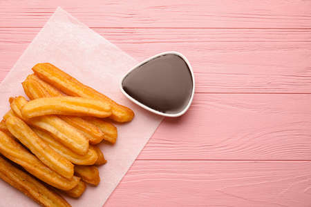 Parchment with tasty churros and melted chocolate sauce on color wooden backgroundの写真素材