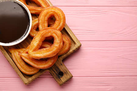 Board with tasty churros and melted chocolate sauce on color wooden backgroundの写真素材