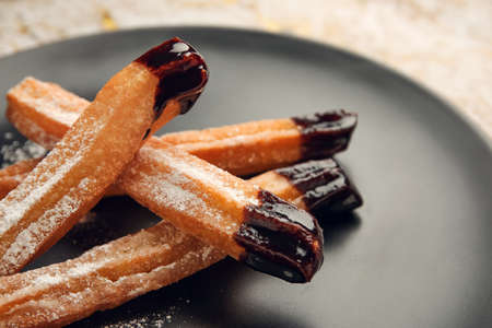 Plate with tasty churros dipped in chocolate, closeup