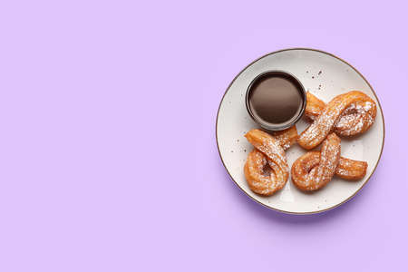 Plate with tasty churros and melted chocolate sauce on color background