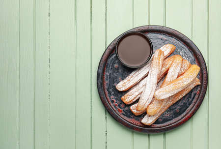 Plate with tasty churros and melted chocolate sauce on color wooden background