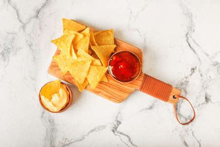 Board with tasty nachos and sauces on light background