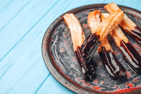 Plate with tasty churros dipped in chocolate on color wooden background, closeupの写真素材