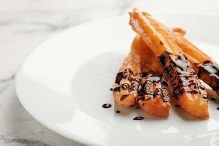 Plate with tasty churros dipped in chocolate on light background, closeup