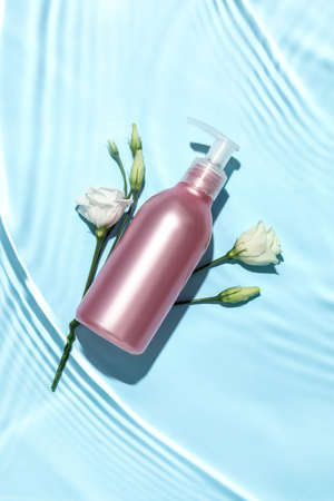 Bottle of cosmetic product and flowers in water on color backgroundの写真素材