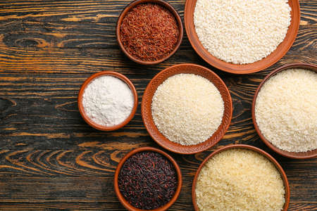 Bowls with different types of raw rice on wooden backgroundの写真素材