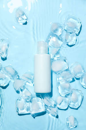 Bottle of cosmetic product and ice cubes in water on color backgroundの写真素材