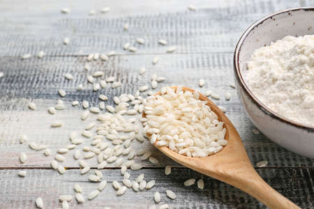 Bowl with flour and spoon with raw rice on wooden background