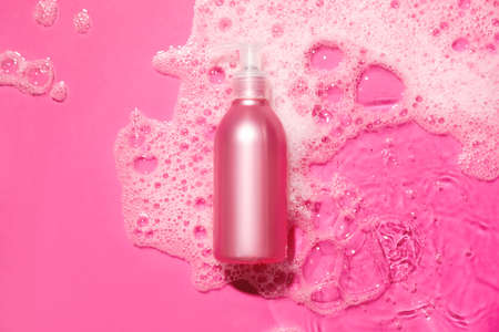 Bottle of cosmetic product in water with foam on color backgroundの写真素材