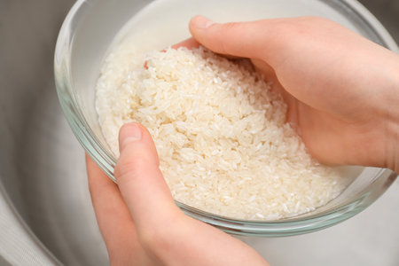 Woman rinsing rice in glass bowl under running water, closeupの写真素材