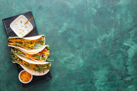 Plate with tasty tacos and sauce on color background
