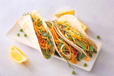 Plate with tasty tacos and lemon on light background
