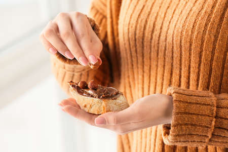 Woman eating bread with tasty chocolate paste and hazelnuts, closeupの写真素材