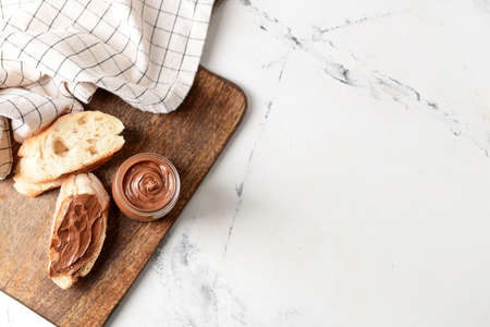 Bowl with tasty chocolate paste and hazelnuts on light background