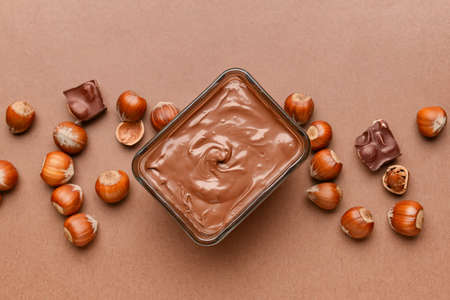 Bowl with tasty chocolate paste and hazelnuts on color backgroundの写真素材