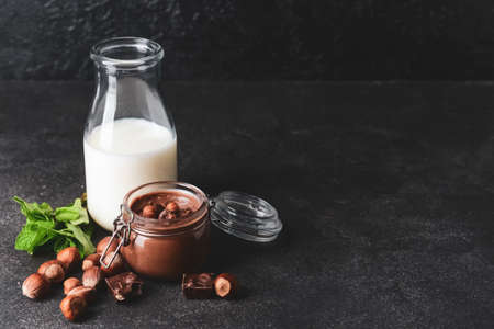 Jar with tasty chocolate paste, hazelnuts and bottle of milk on dark backgroundの写真素材