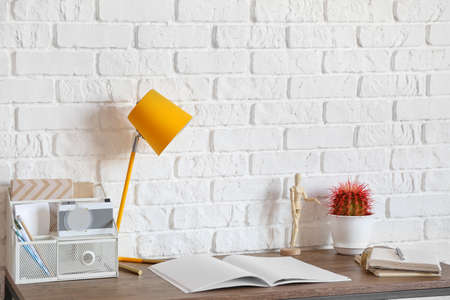 Table with lamp, organizer and notebooks near brick wallの写真素材
