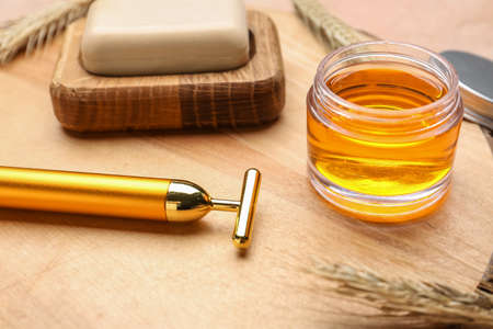 Facial massage tool with essential oil and soap on wooden board, closeup