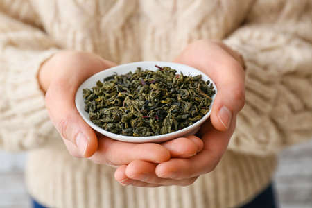 Woman holding bowl with dry green tea leaves, closeupの写真素材