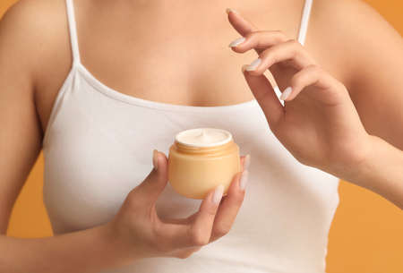 Young woman with facial cream on color background, closeup