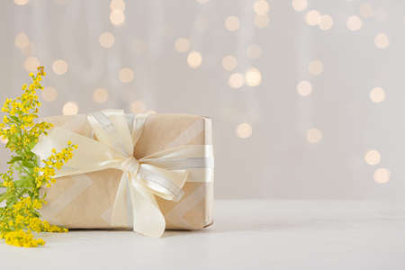 Gift box and beautiful flowers on table against blurred lightsの写真素材