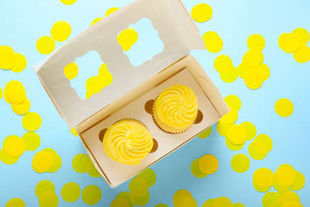 Box with tasty cupcakes and confetti on color background