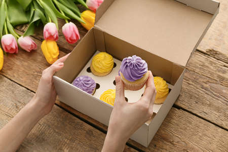Female hands with tasty cupcakes in box on wooden backgroundの写真素材