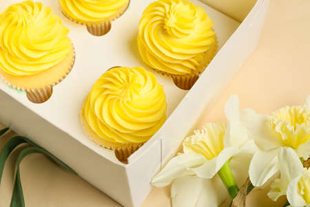 Box with tasty cupcakes and narcissus flowers on color backgroundの写真素材