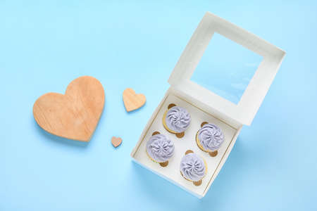 Box with tasty cupcakes and wooden hearts on color background