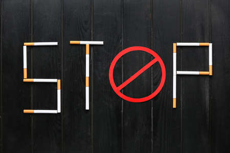 Word STOP made of cigarettes on dark wooden background