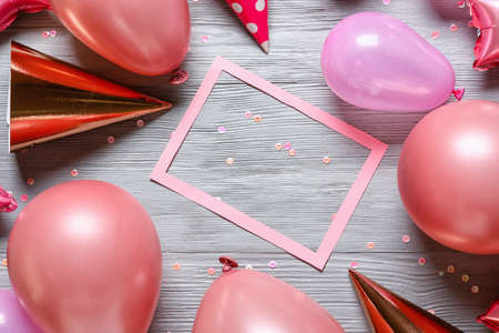 Composition with paper frame, air balloons and party hats on gray wooden background