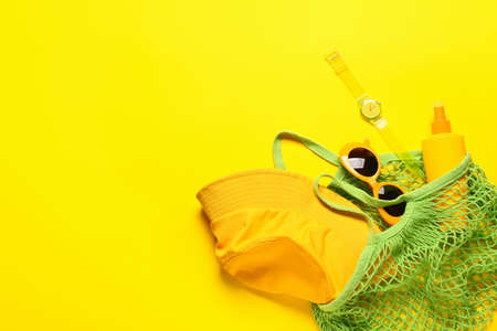 Bag with beach accessories on color background
