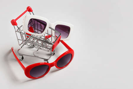 Shopping cart with stylish sunglasses on gray background