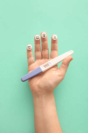 Woman holding pills with drawn faces and pregnancy test on color background, closeup