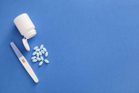 Bottle of pills and pregnancy test on color background