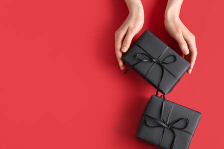 Hands with black gift boxes on color background