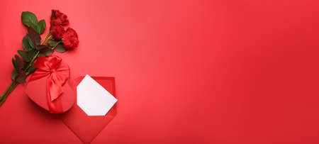 Gift box for Valentine's Day with envelope, letter and roses on red background with space for textの写真素材
