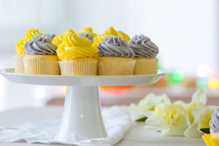 Dessert stand with tasty cupcakes and beautiful narcissus flowers on table