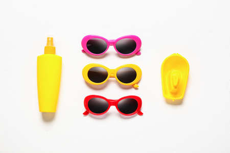 Stylish sunglasses, bottle of sunscreen and toy boat on white background