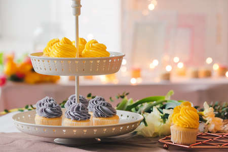 Dessert stand with tasty cupcakes and flowers on table