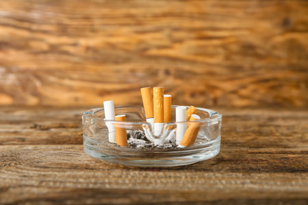 Ash tray with cigarettes on wooden background